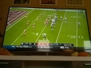 A TV showing a football play from behind the line of scrimmage, with the score bar along the bottom