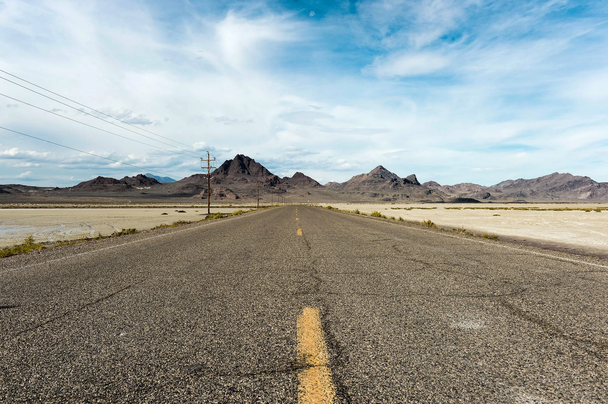 A straight two-lane road running toward desert mountains across flat salt flats, seen from road level