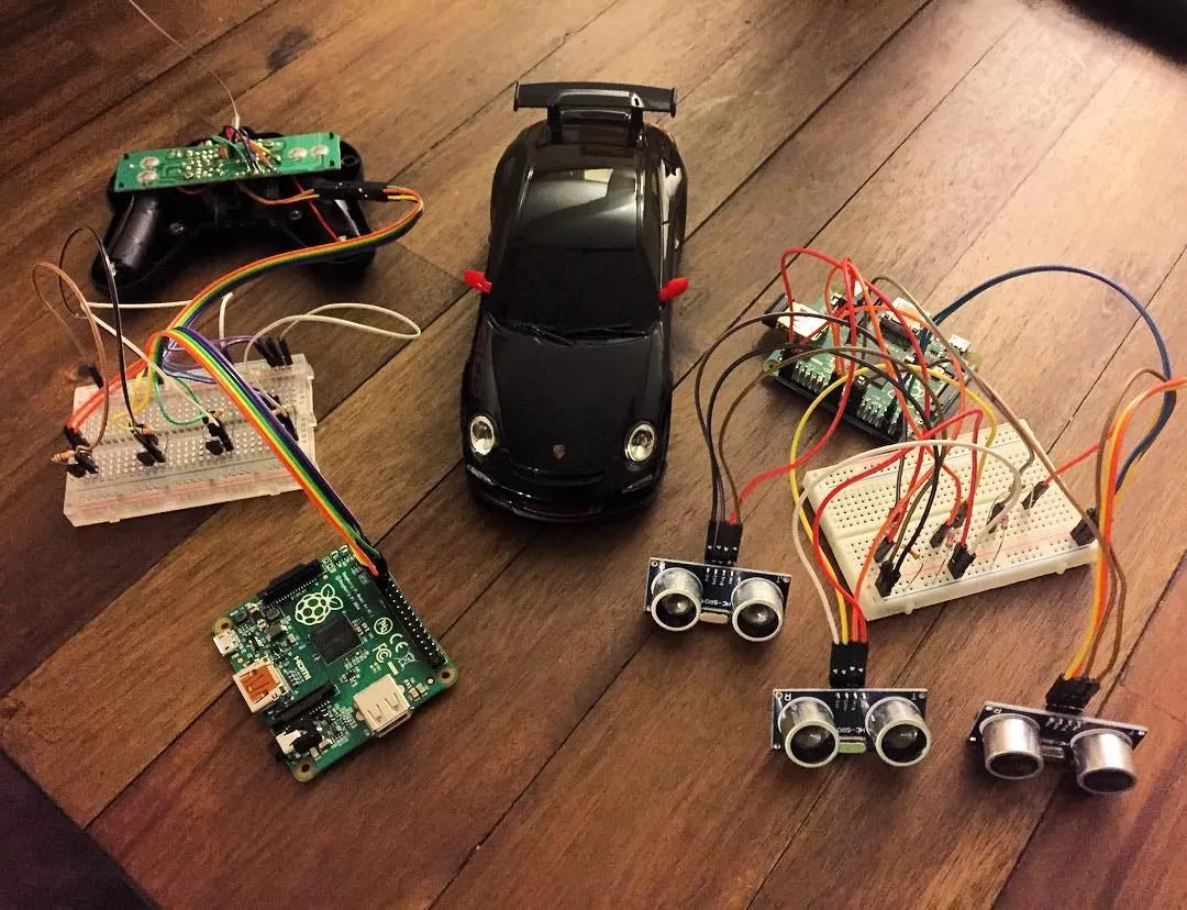 Hardware on a wooden table: a black toy Porsche 911 GT3 in the middle, a Raspberry Pi wired to an opened remote control on the left, and a second Raspberry Pi on a breadboard wired to three ultrasonic sensors on the right