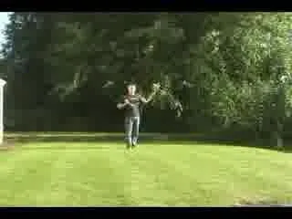 Video frame of a person on a lawn swinging nunchucks in front of trees