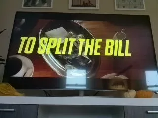 A TV showing an ad with the words “To split the bill” in bold yellow letters