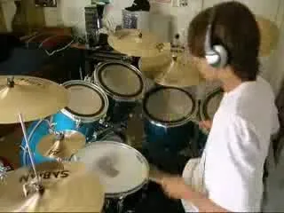 Video frame of a boy wearing headphones playing a drum kit