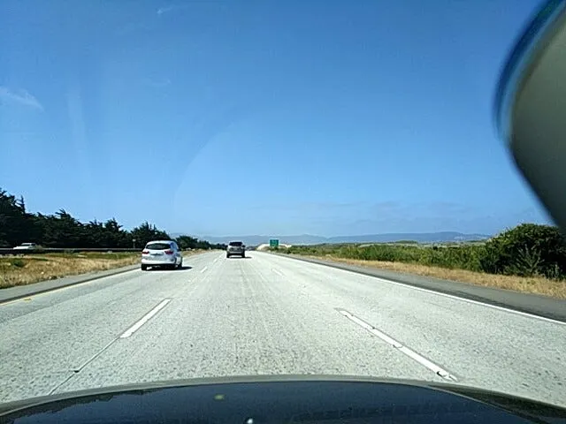 Dashcam view of a nearly empty highway under a blue sky, with the edge of the mount at the right