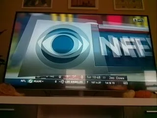 A TV showing a large CBS and NFL logo graphic over the game, with the score bar along the bottom