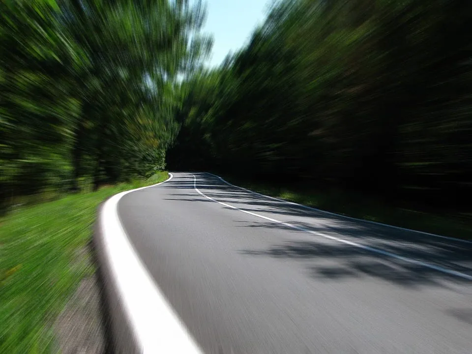 A winding road through green trees with heavy radial motion blur, as if seen at high speed