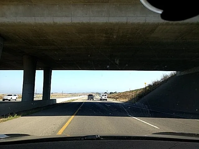 Dashcam view of a highway passing under a concrete overpass, with the mount visible at the top