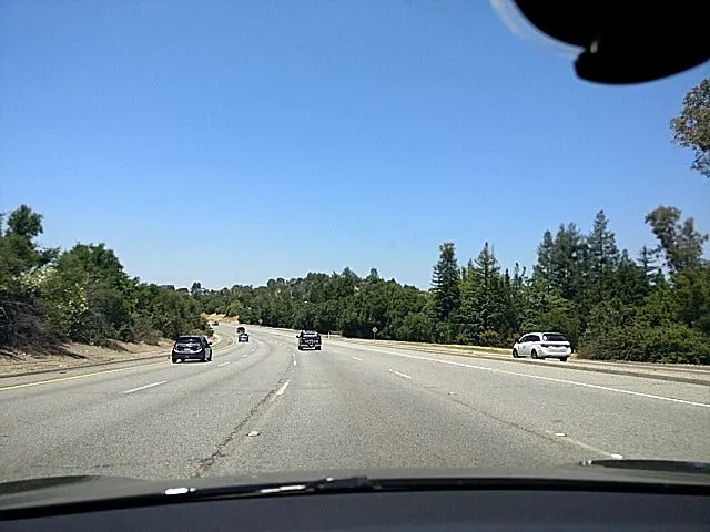 Dashcam view of an open highway lined with trees under a clear sky